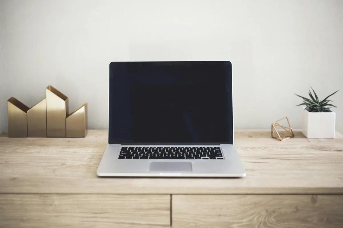 Open MacBook laptop on a wooden desk beside a coffee cup and notebook