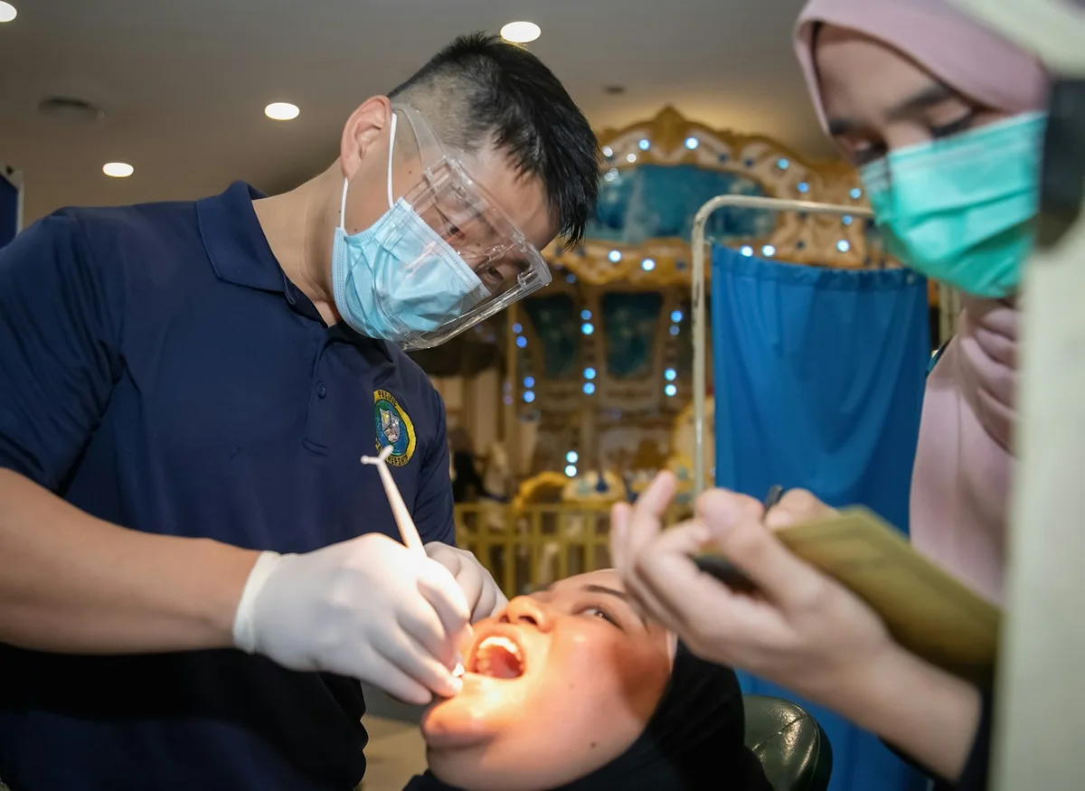 Dental treatment chair and overhead lamp in a clinical exam room with dentist and assistant