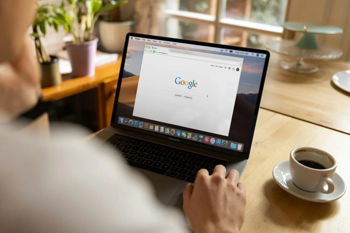 Person typing on a MacBook keyboard at a wooden desk with a plant nearby