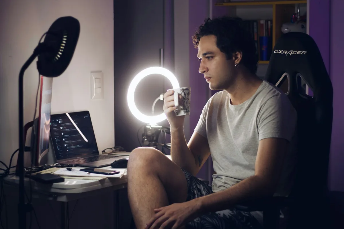 Man in a grey t-shirt seated on a chair filming himself with a phone on a stand