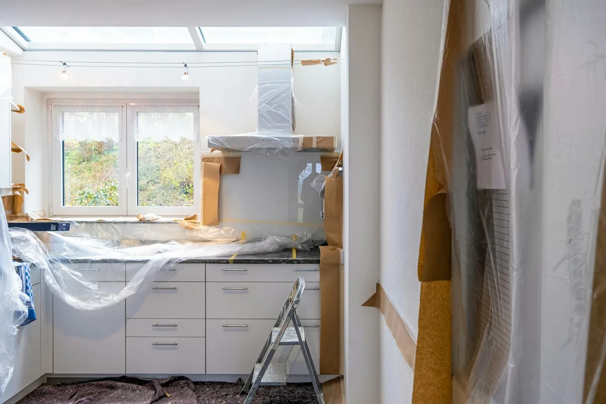 Kitchen mid-renovation with plastic-wrapped white cabinets and brown protective paper on the floor