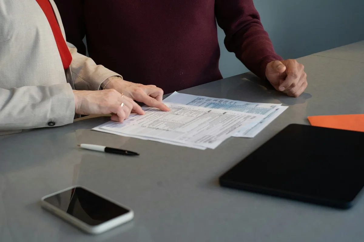 Two people reviewing a printed loan application form at a desk beside a phone and a tablet