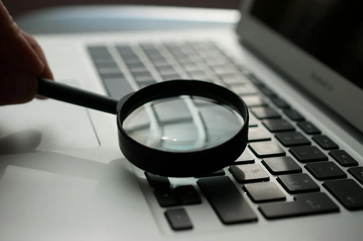 Close-up of a magnifying glass held over a laptop keyboard on a wooden desk