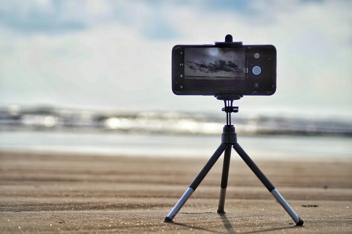 Smartphone standing upright on a stone beach with sea and cloudy sky behind it