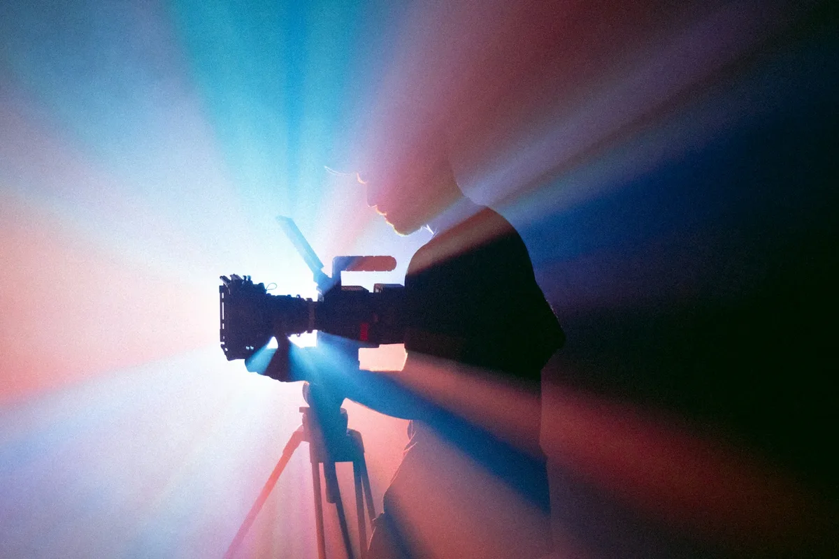 Person operating a video camera on a tripod under blue and red studio lighting